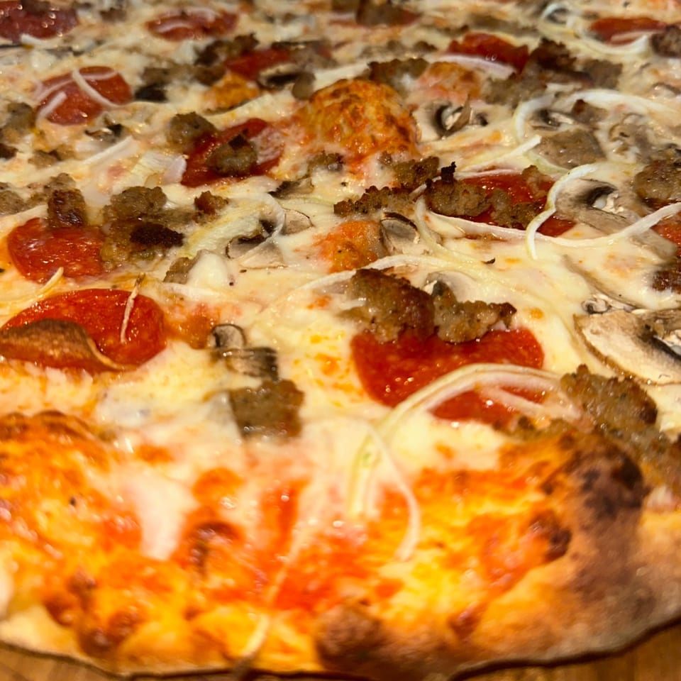 A close-up of a hot Amore Pizza with pepperoni, sausage, mushrooms, and onions.