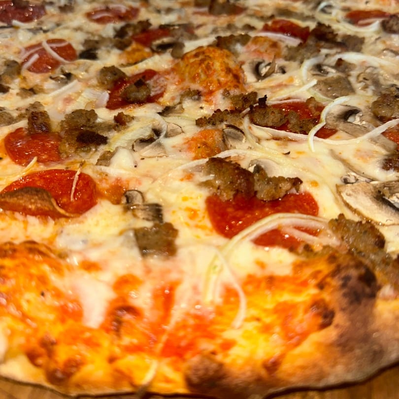 A close-up of a hot Amore Pizza with pepperoni, sausage, mushrooms, and onions.