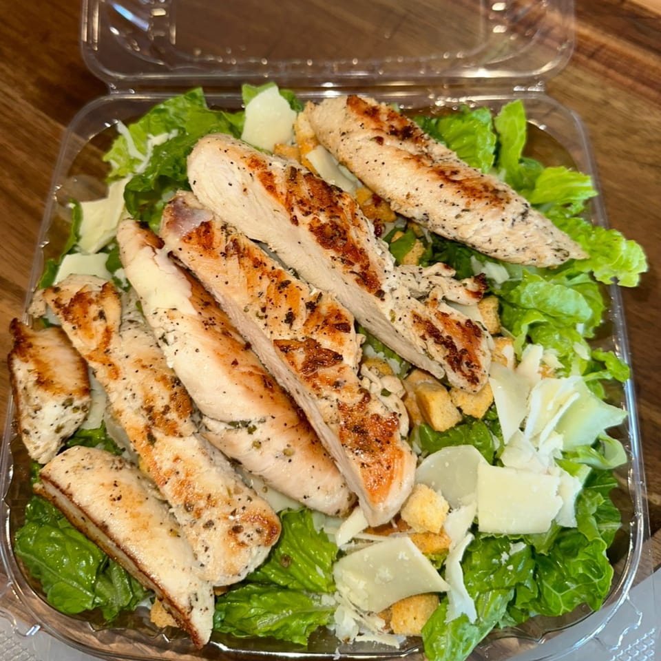 Amore Pizza & Subs Caesar salad with grilled chicken, croutons, and Parmesan cheese in a plastic container.