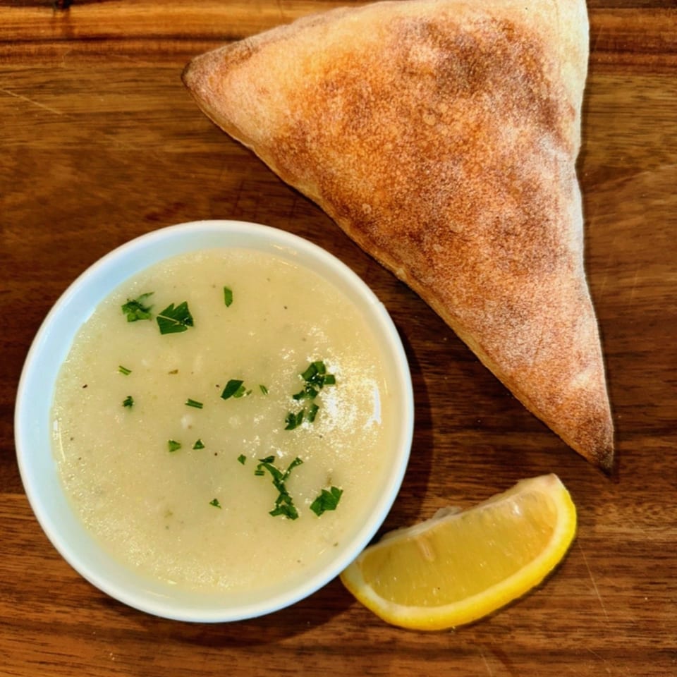 Amore Pizza & Subs' creamy soup with parsley, a lemon wedge, and a slice of bread on wood.
