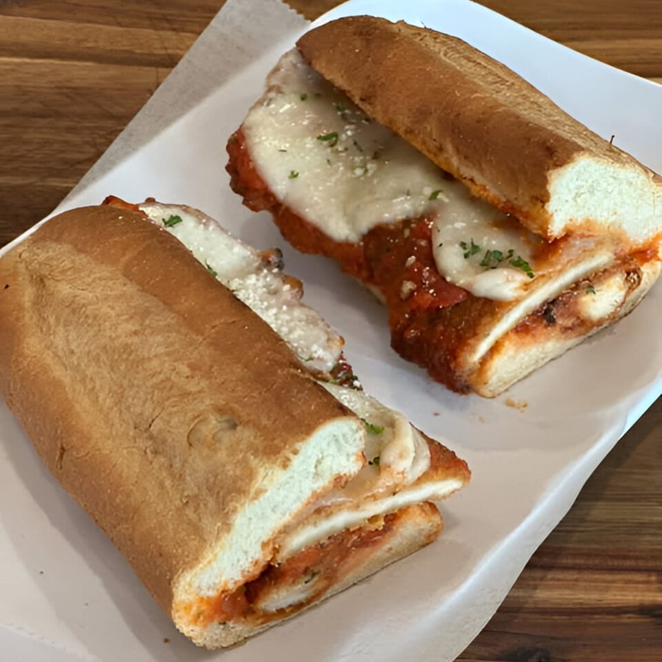 Two Amore Pizza & Subs chicken parmesan subs with melted cheese and sauce on a white plate.